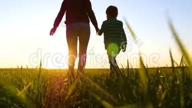 一位<strong>年轻</strong>的<strong>母亲牵</strong>着儿子`手，在美丽的夕阳下穿过绿草。